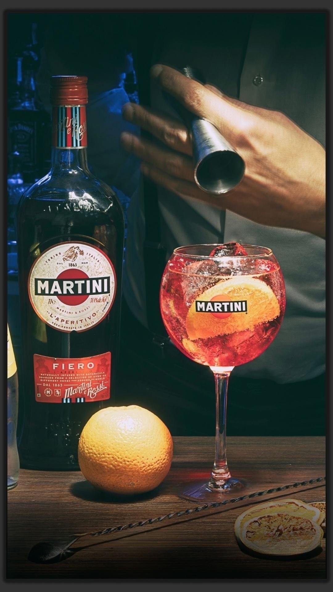 Un cocktail preparato al bancone, con arancia e bottiglia di Martini